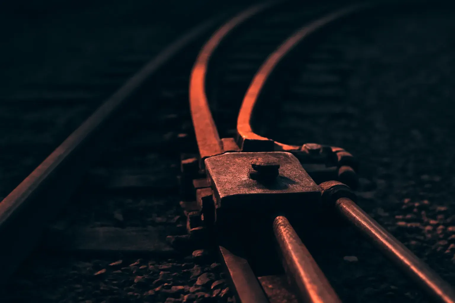 Duotone graphite and vermilion macro photograph of a railway track switch where two rails diverge from one.
